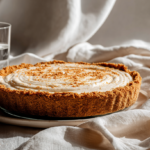 Whole Butterfinger cream pie in graham cracker crust on white cloth with a glass of water